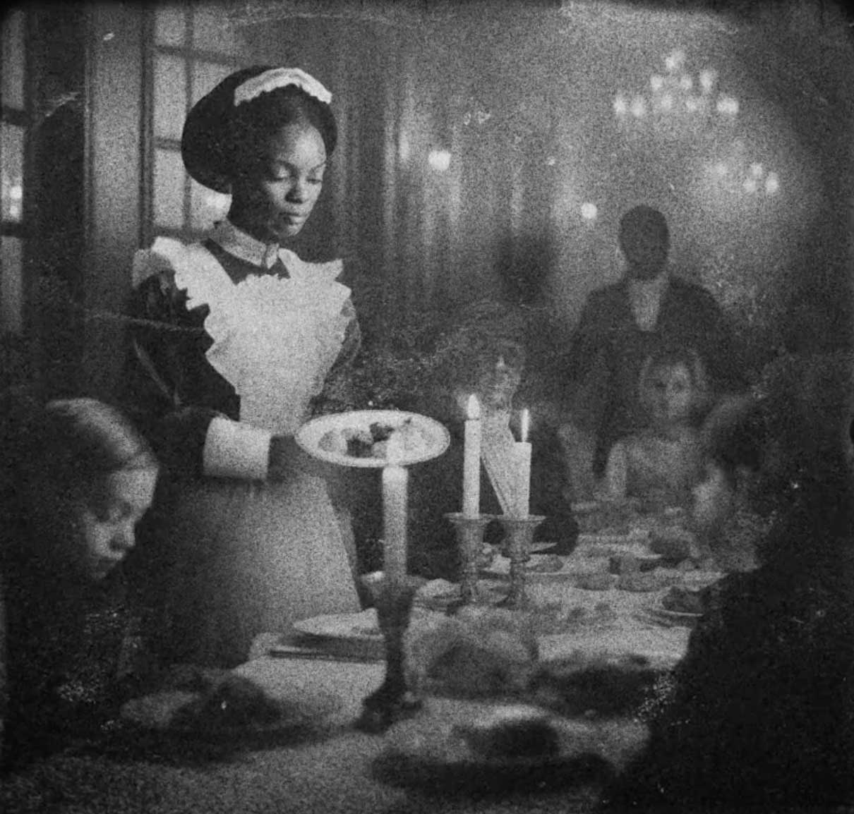 Film still of woman serving dinner table. 